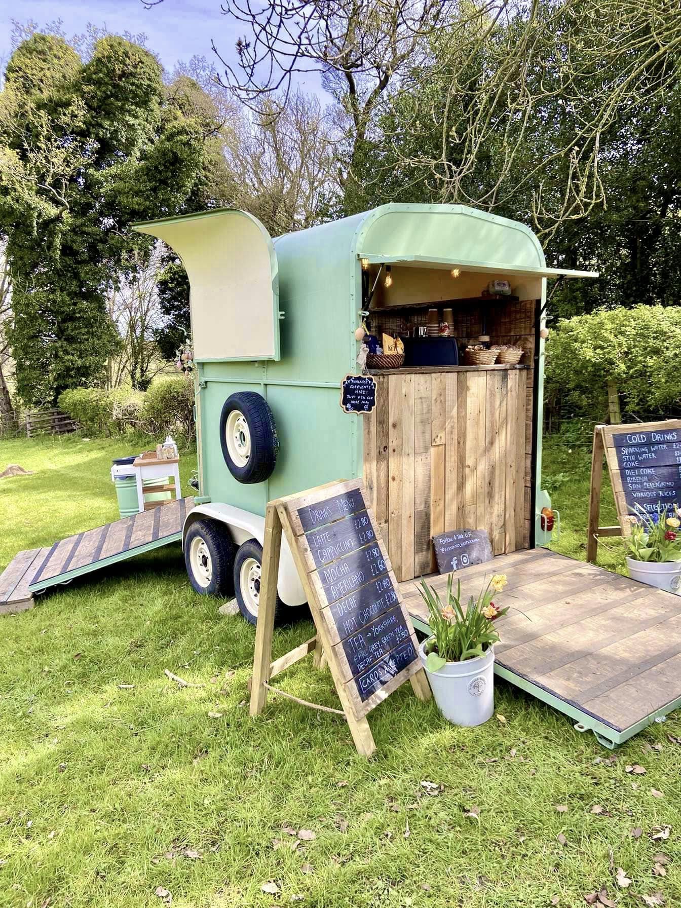Elevenses café — a charming mint green converted horsebox with a wooden serving counter, fairy lights, and a handwritten chalkboard menu